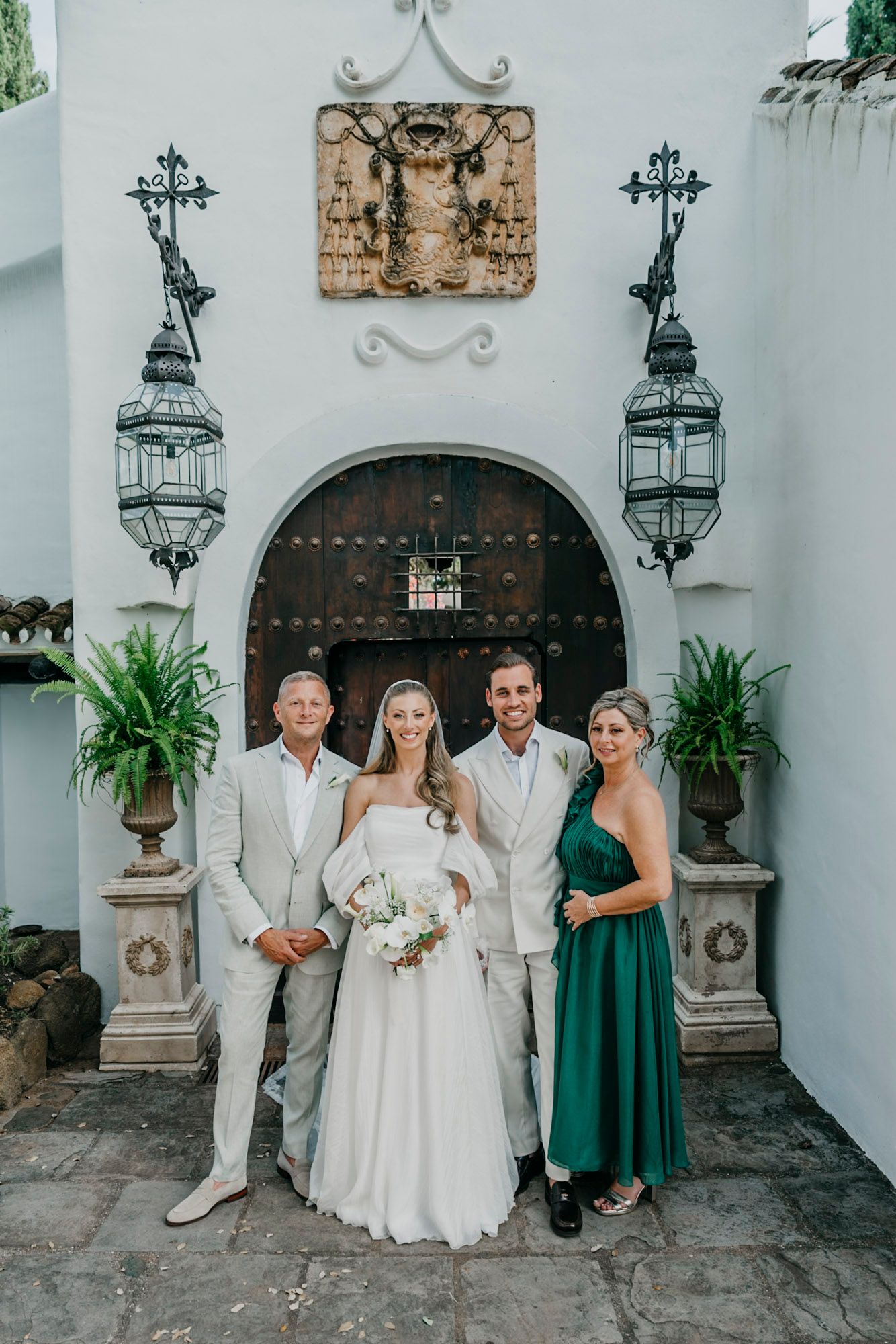Wedding party poses against white Spanish colonial style building with ornate lanterns.