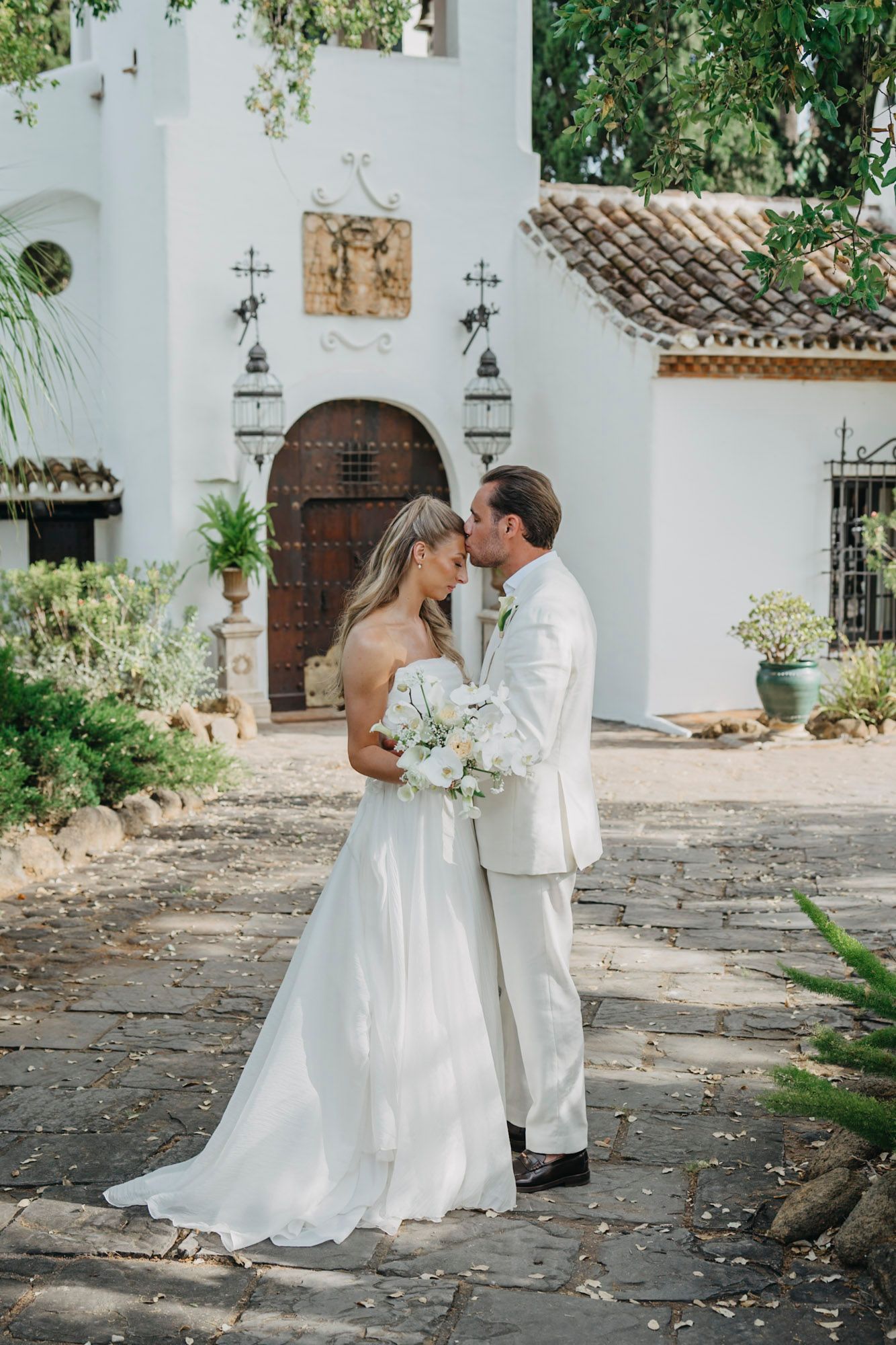 Romantic moment outside Spanish mission-style church with white walls.