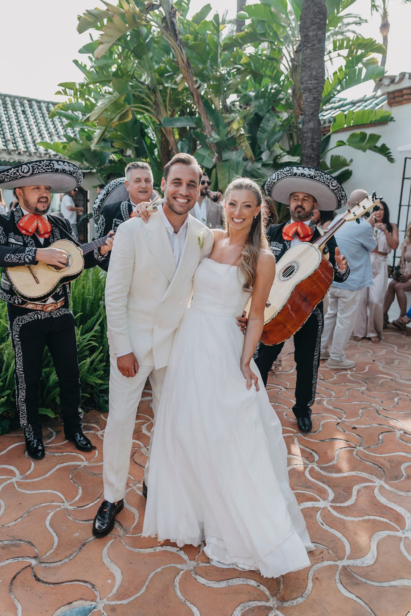 Wedding celebration with mariachi band performing in tropical garden setting.