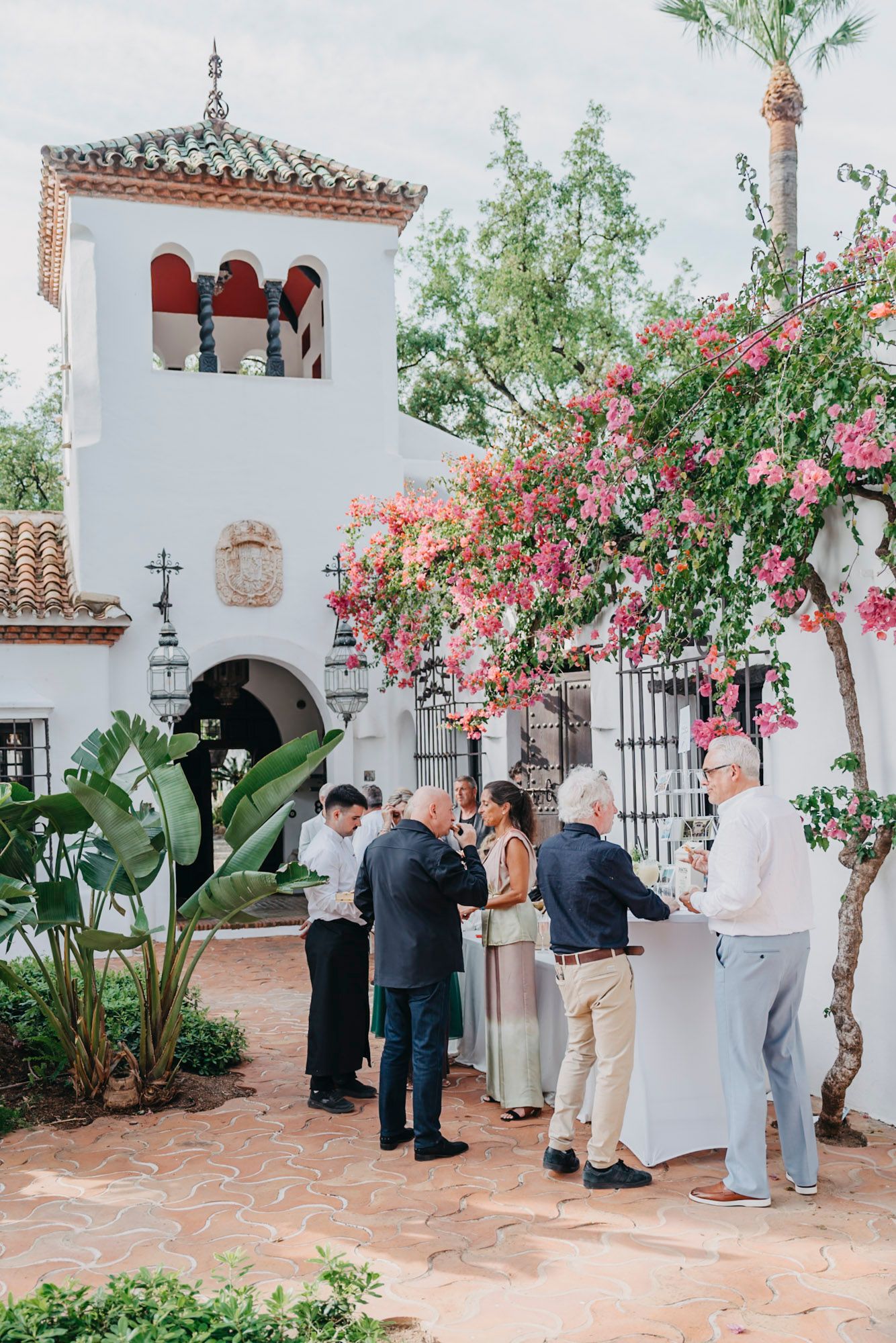 Wedding guests gather in a Mediterranean courtyard with pink bougainvillea and white stucco walls.