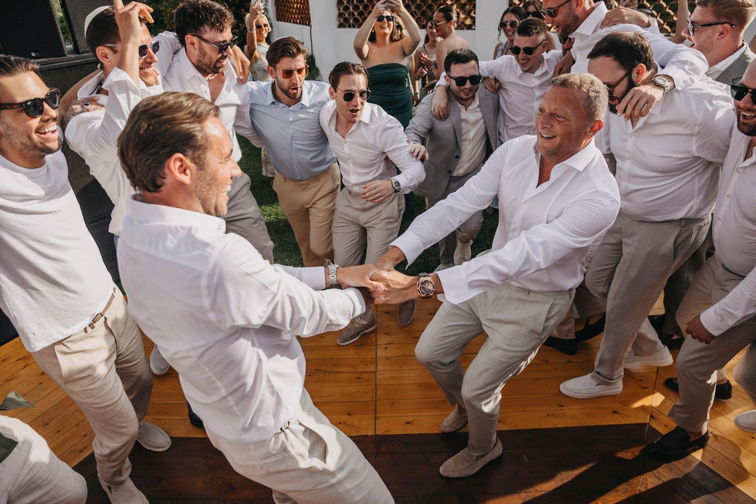 Wedding party dancing and celebrating energetically on a wooden dance floor.
