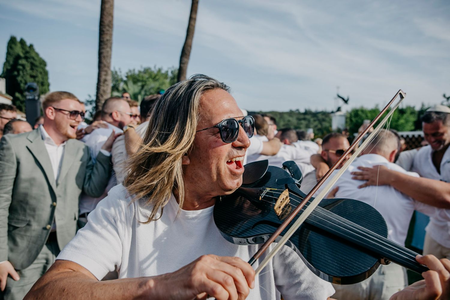 Wedding guests enjoying outdoor festivities under blue skies with musical entertainment.