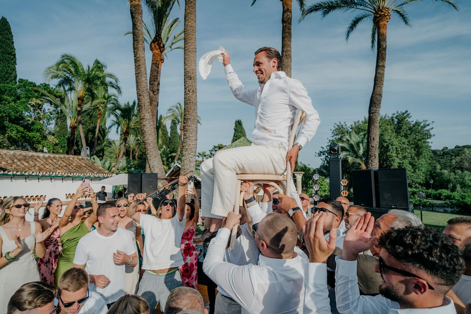 Wedding celebration with guests dancing and enjoying festivities under palm trees at an outdoor tropical venue.