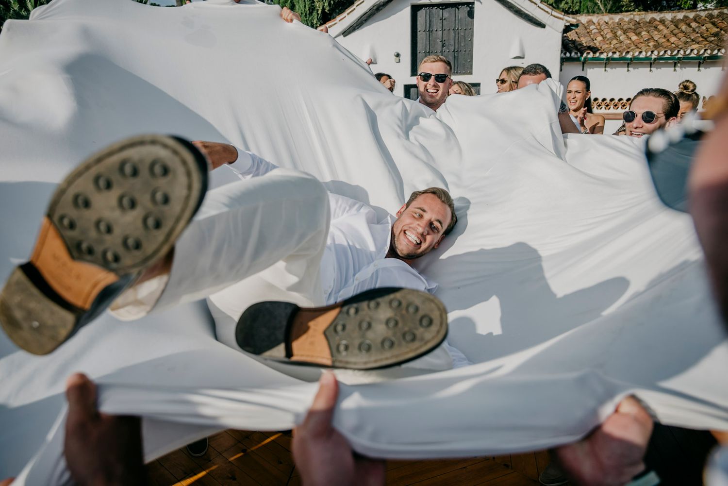 Wedding guests being lifted and tossed in celebration during outdoor reception.