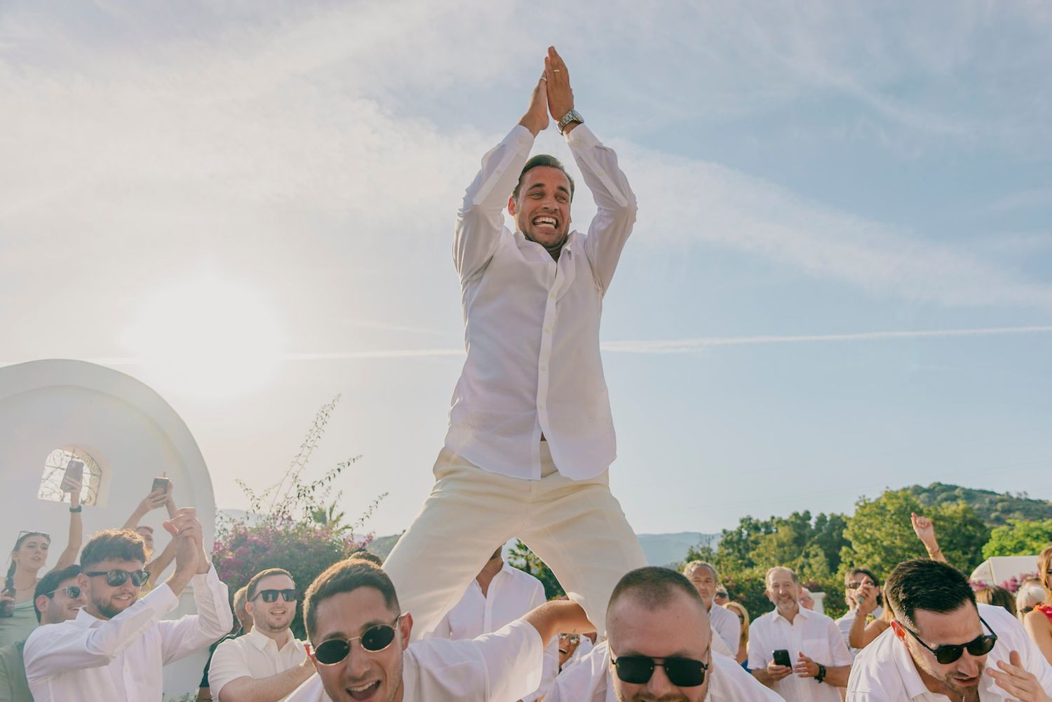 Wedding guests celebrate and dance together at an outdoor reception under blue skies.