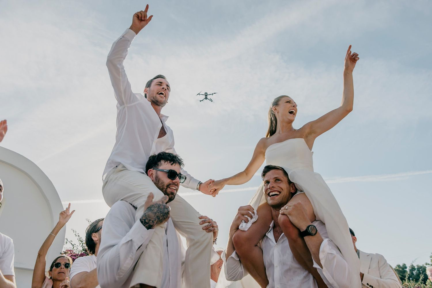 Joyful wedding guests jumping and celebrating against a bright blue sky.