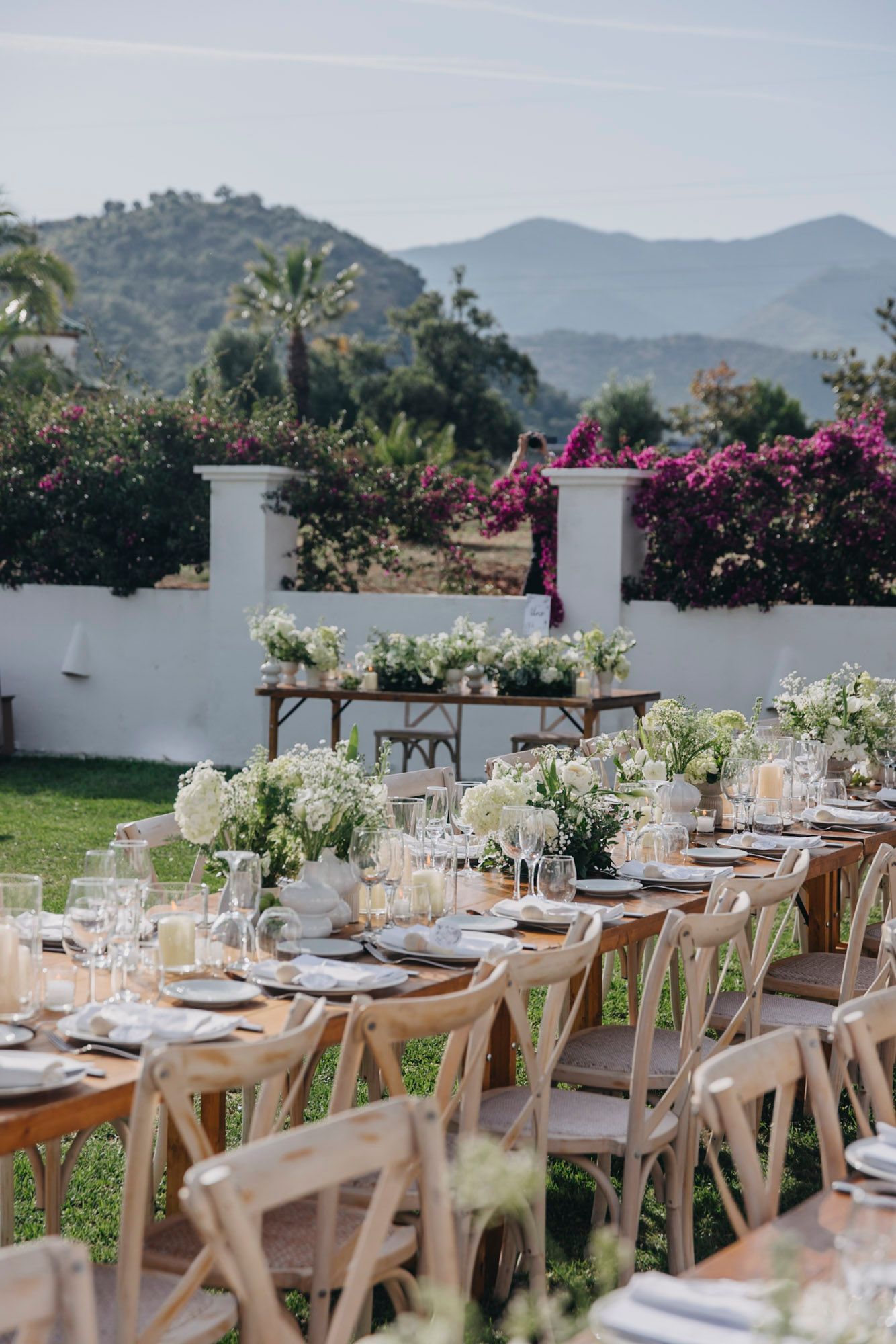 Elegant outdoor wedding reception setup with mountain views and rustic wooden tables decorated with white florals.