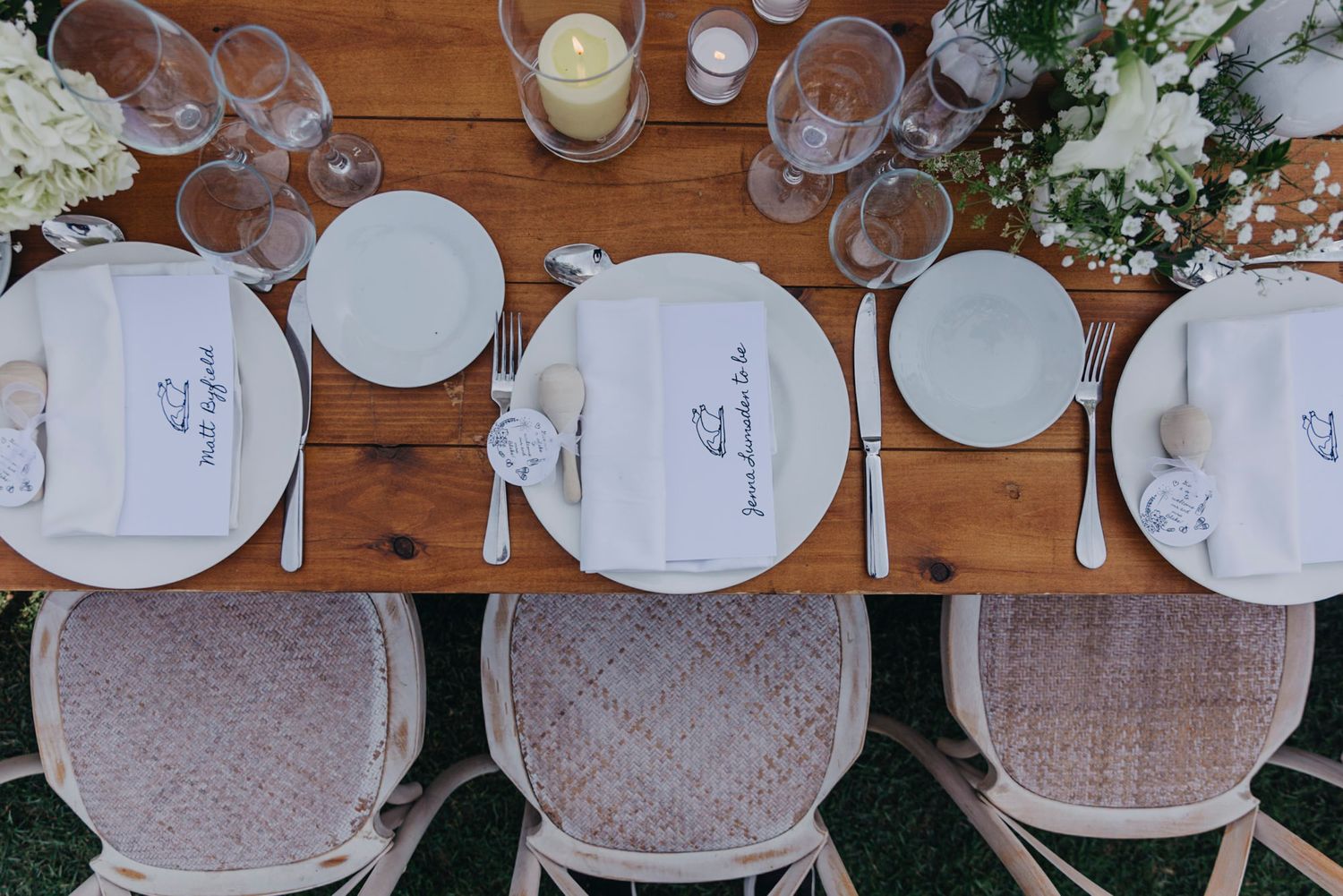 Elegant table setting with white plates and glassware on rustic wooden tables.