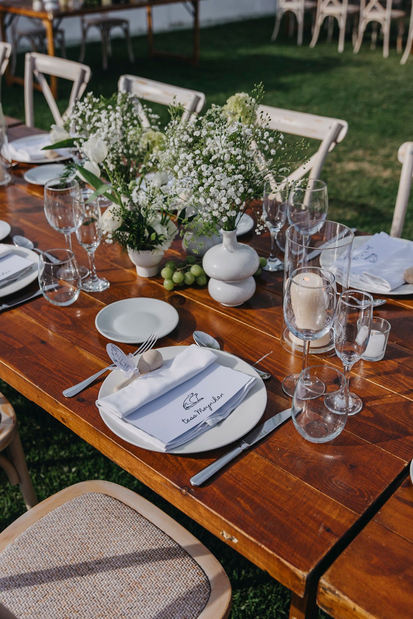 Rustic outdoor wedding reception table with white place settings and delicate floral centerpieces.