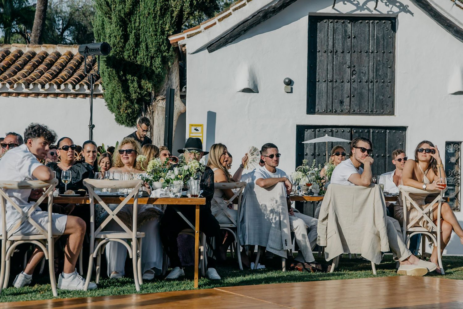 Outdoor wedding venue with white building and guests seated in garden setting.