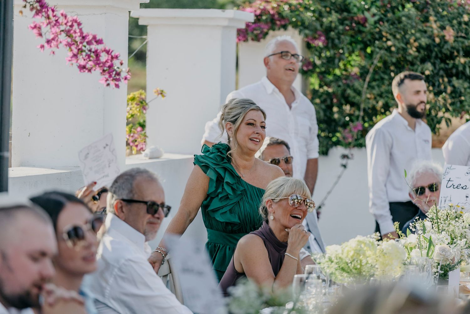 Wedding guests in white attire enjoying an outdoor garden reception with pink bougainvillea flowers.