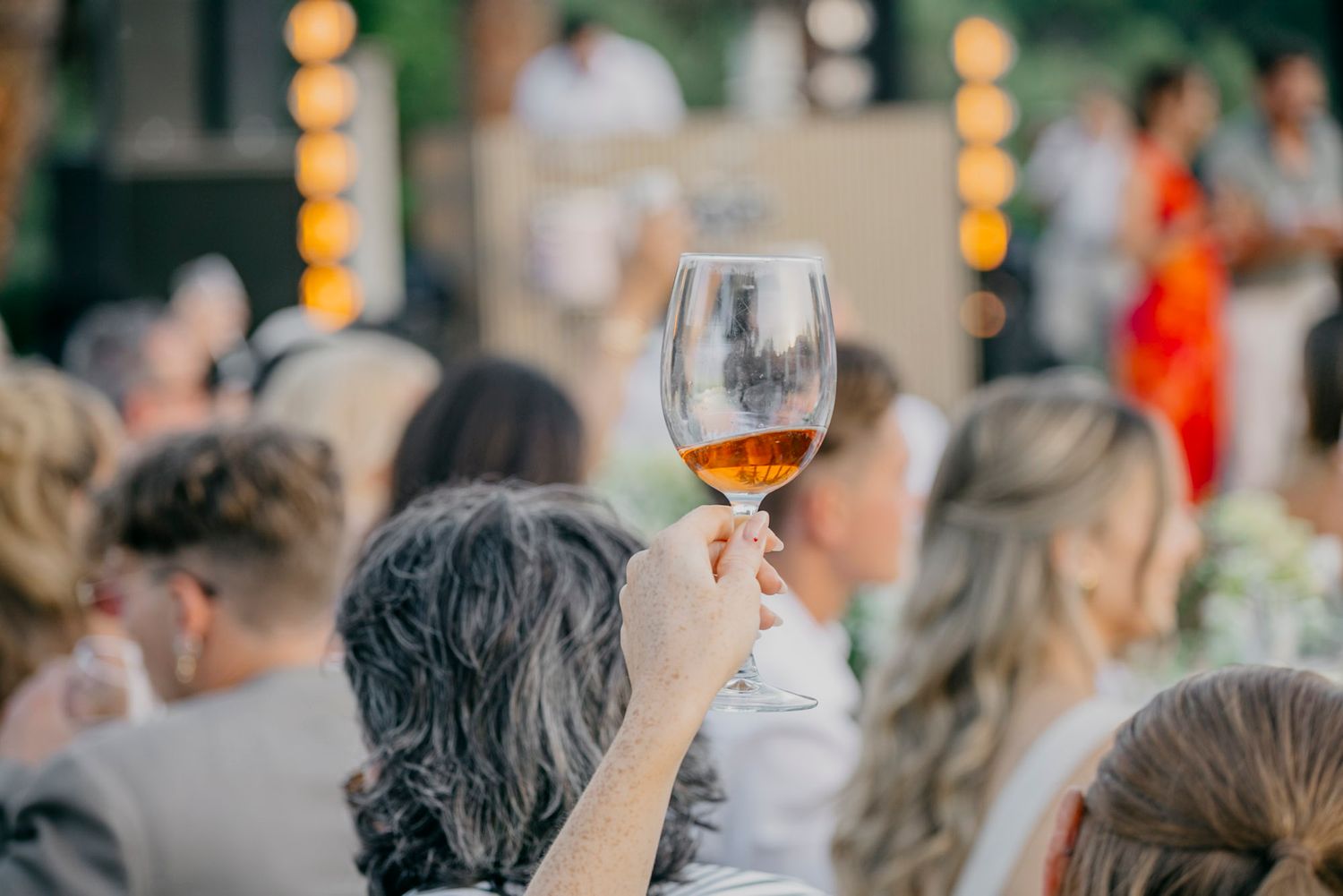 A row of people holding wine glasses at an outdoor tasting event during sunset.