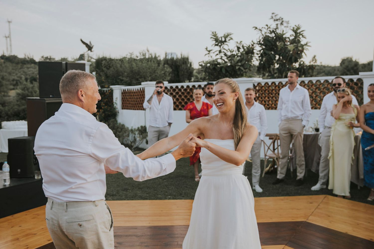 A couple dances together on an outdoor wooden dance floor at a daytime wedding reception.