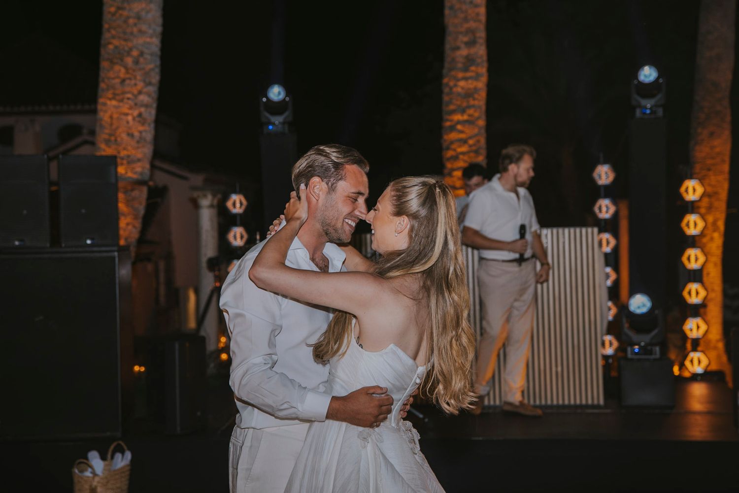 Wedding guests dancing and celebrating at a dimly lit indoor reception venue with warm lighting.