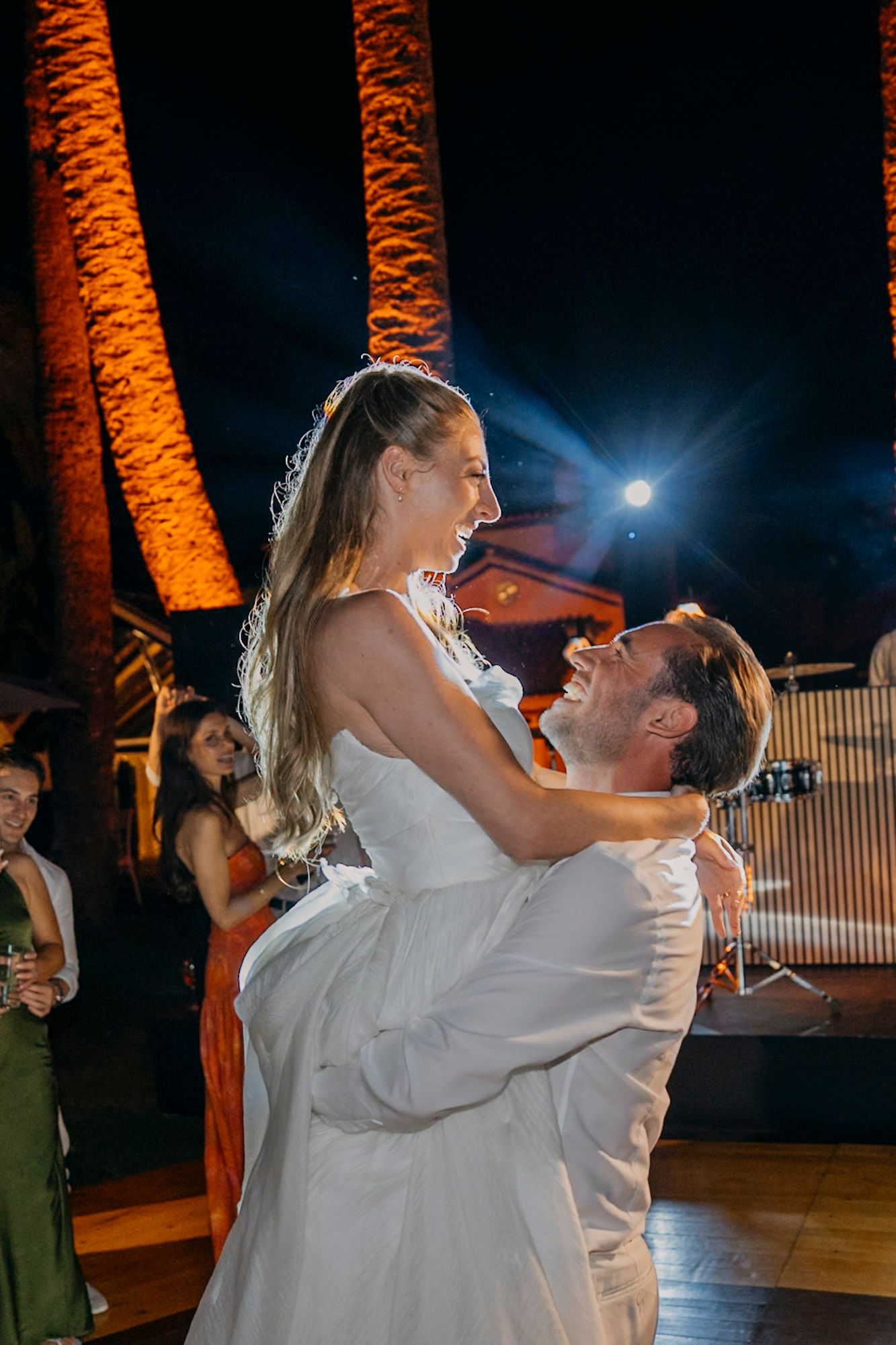 A couple dances together at night under illuminated orange palm trees during a celebration.