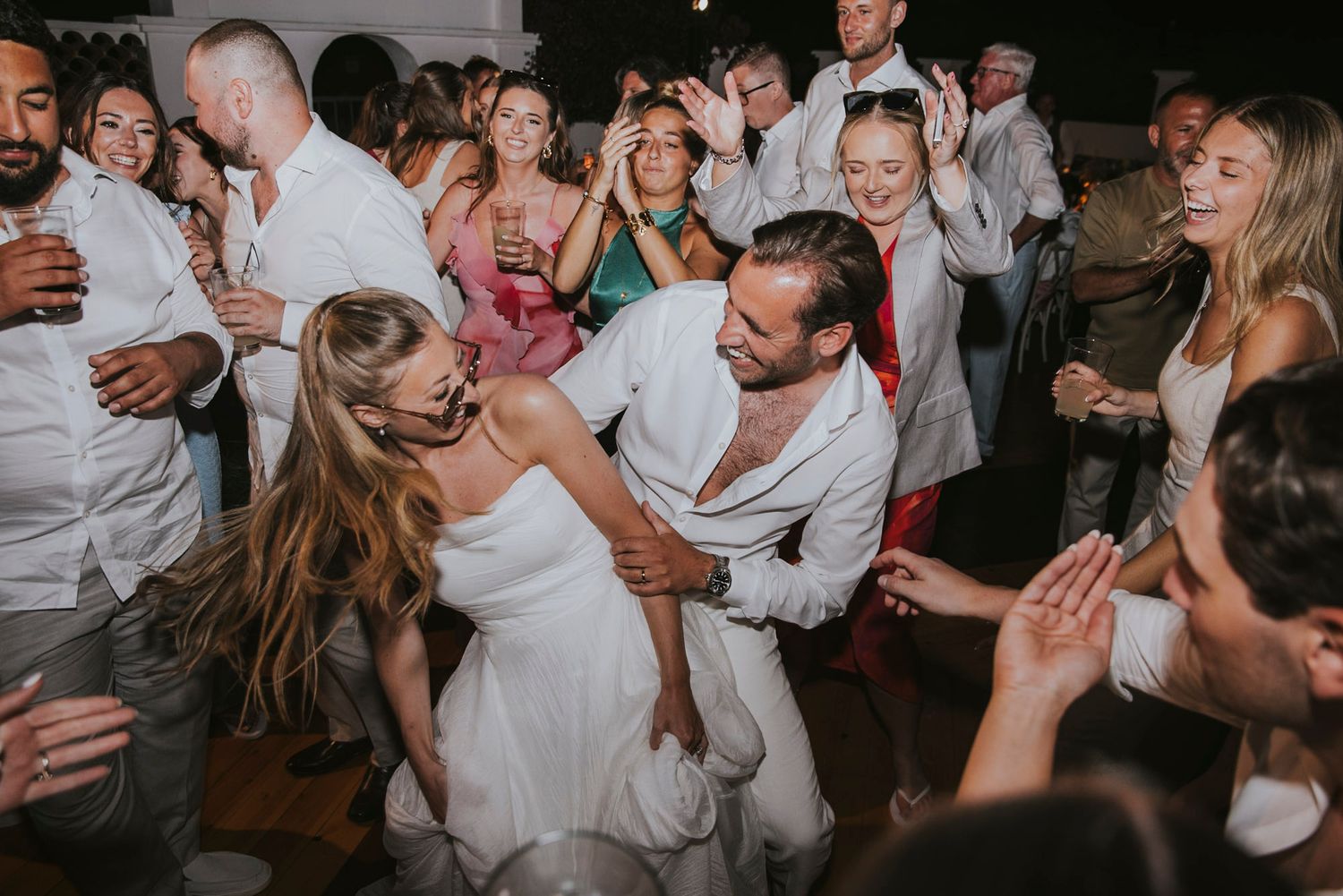Wedding guests dancing and celebrating on a dark dance floor at a reception party.