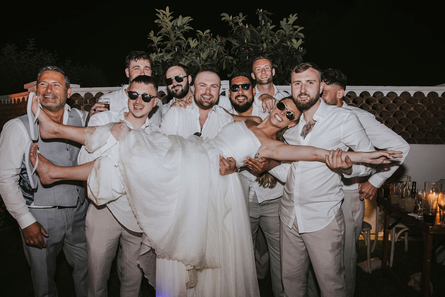Groomsmen in light colored suits posing together at an outdoor wedding celebration.