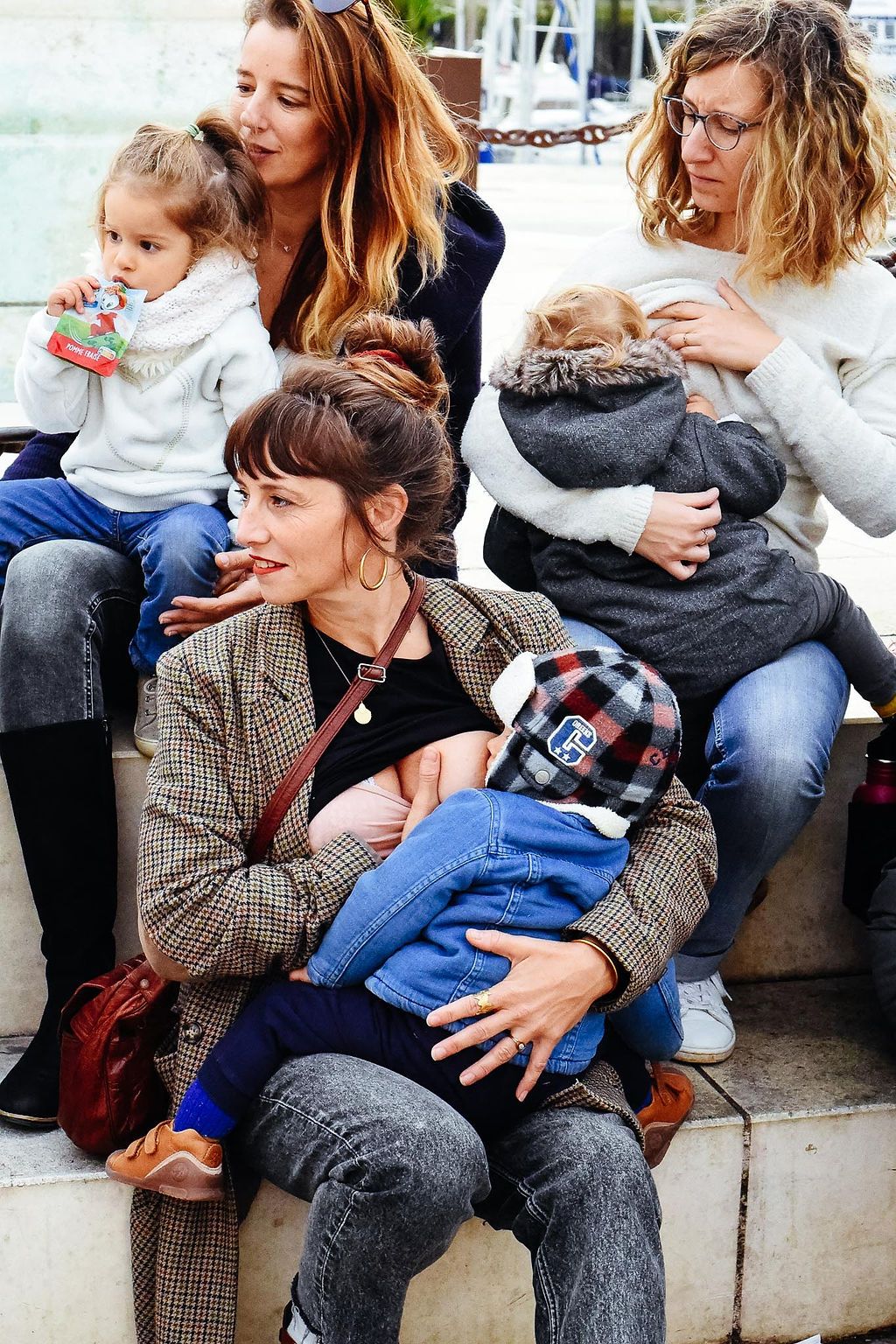 Three adults sitting together with babies and toddlers in casual clothes for a relaxed outdoor family gathering.
