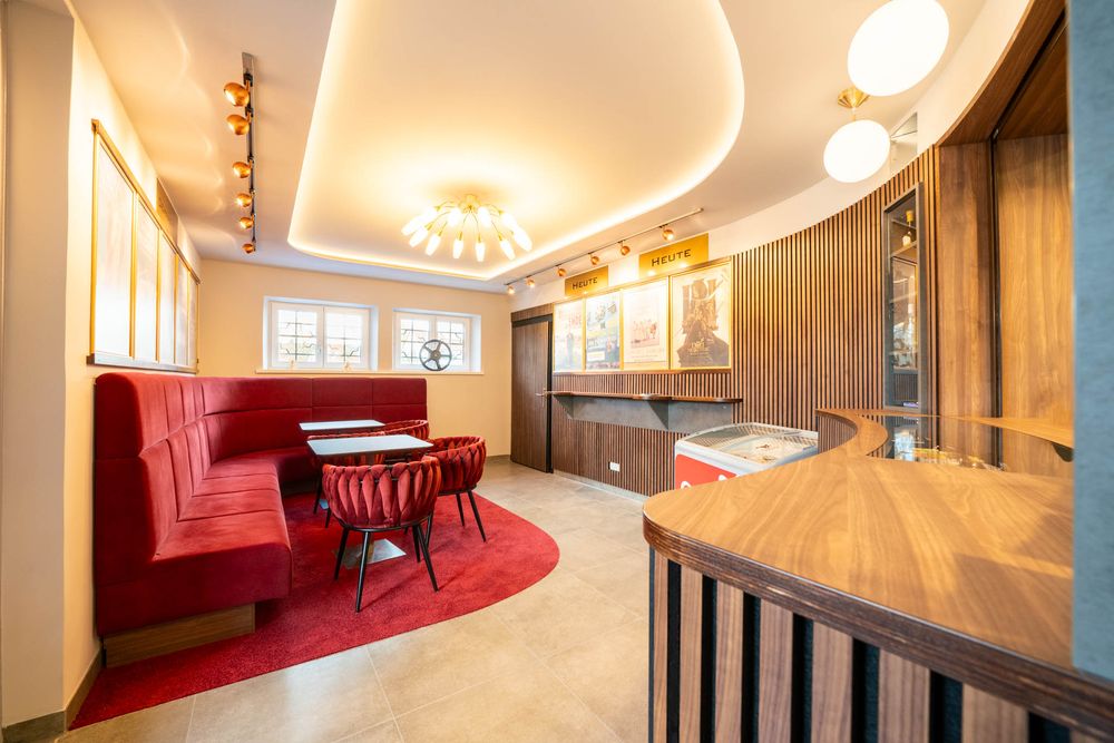 Modern restaurant interior with curved ceiling, red booth seating, and wood paneling illuminated by pendant lights.