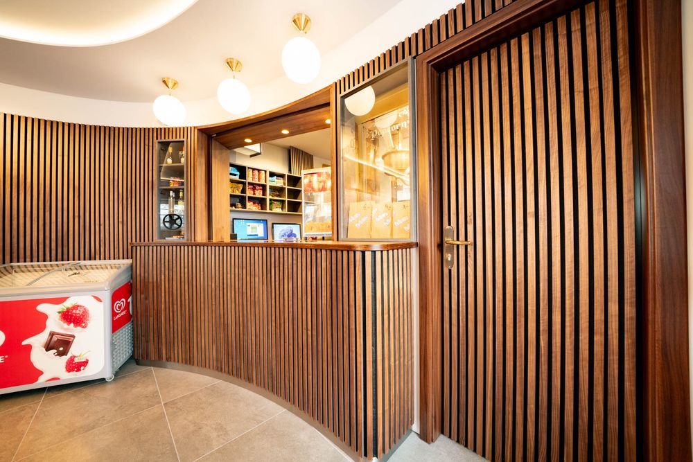 Modern theater lobby with wood paneled walls, chandelier lighting, and red carpet leading down a curved hallway.