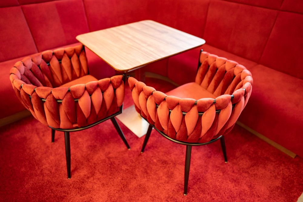 Red velvet chairs and stools arranged in a dimly lit lounge space with moody crimson lighting.