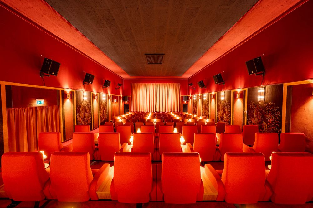 Interior of a nightclub or bar with dramatic red lighting and multiple rooms connected by doorways and hallways.