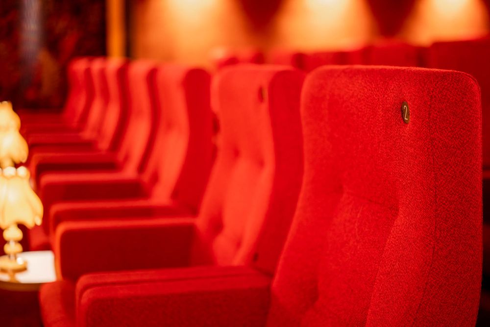 Red theater seats arranged in rows inside a dimly lit auditorium with dramatic red lighting.