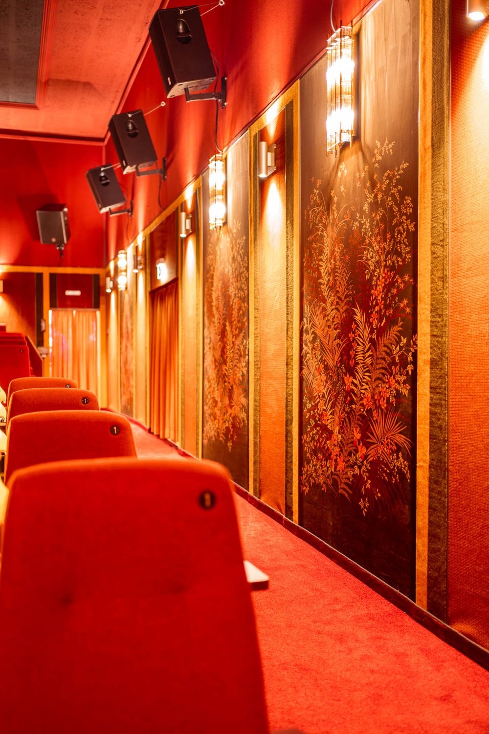 Red-lit hallway with black framed artwork and pendant lights creating a dramatic cinematic atmosphere.