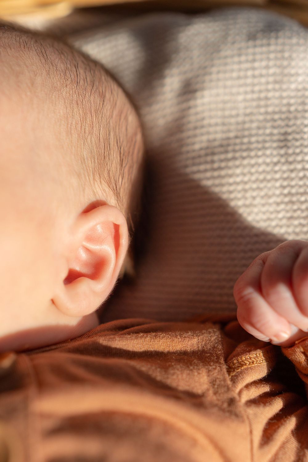 Close-up sequence showing a sleeping baby's ear and side profile against soft brown fabric in natural lighting.