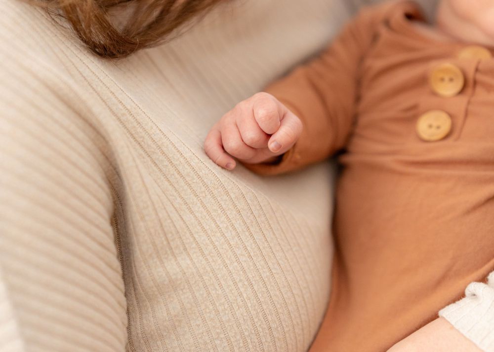 A person wearing a beige sweater holds a baby wearing an orange onesie in a tender moment together.