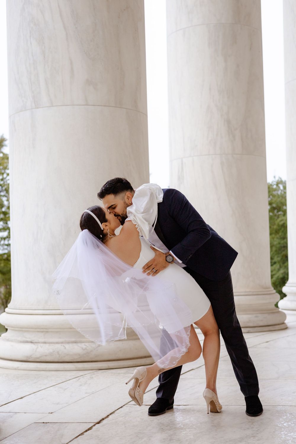 A romantic wedding couple dips in an elegant dance pose between classic white marble columns.