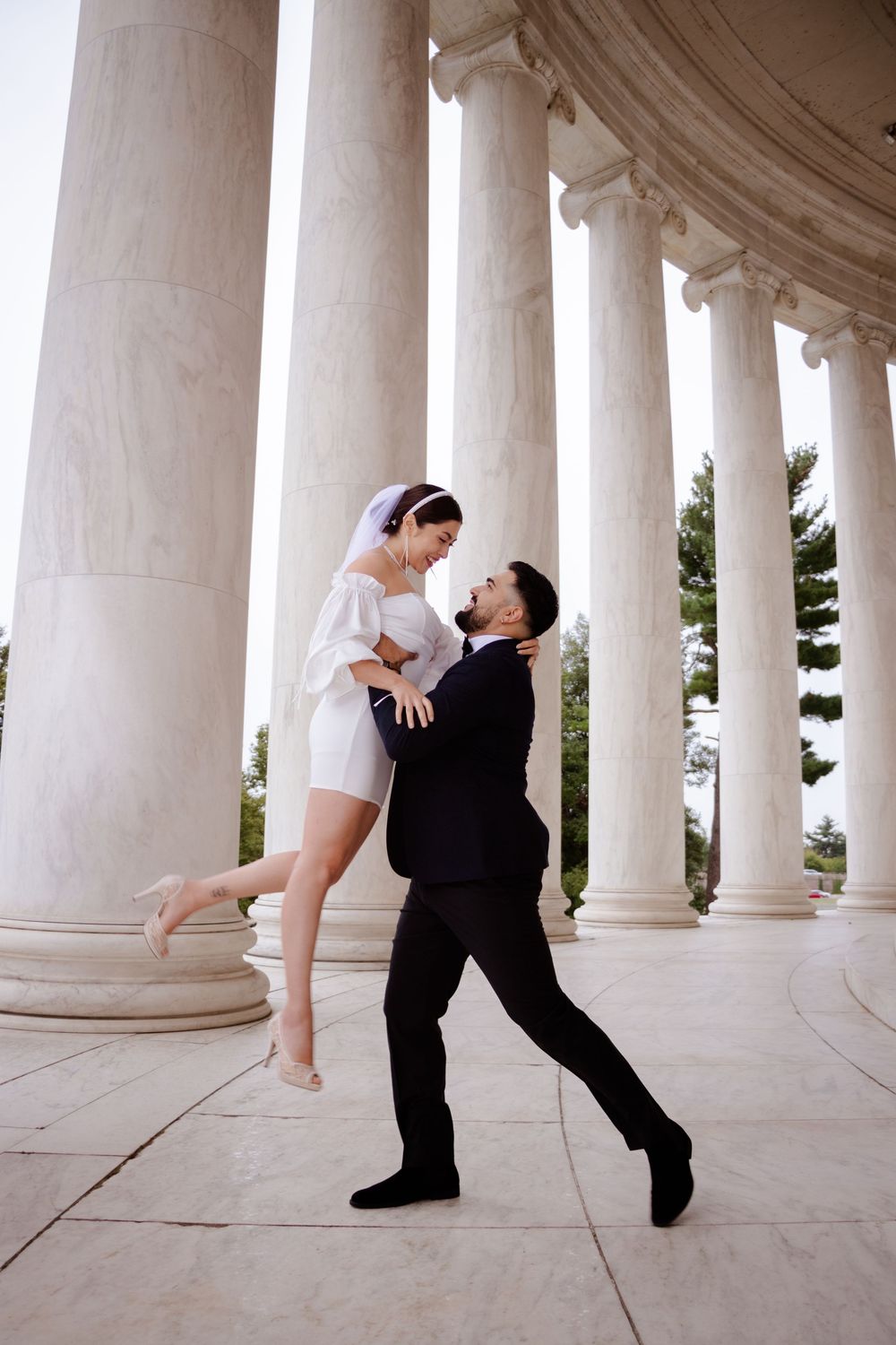 A couple in black and white attire performs a romantic dance sequence under a colonnade of classical columns.