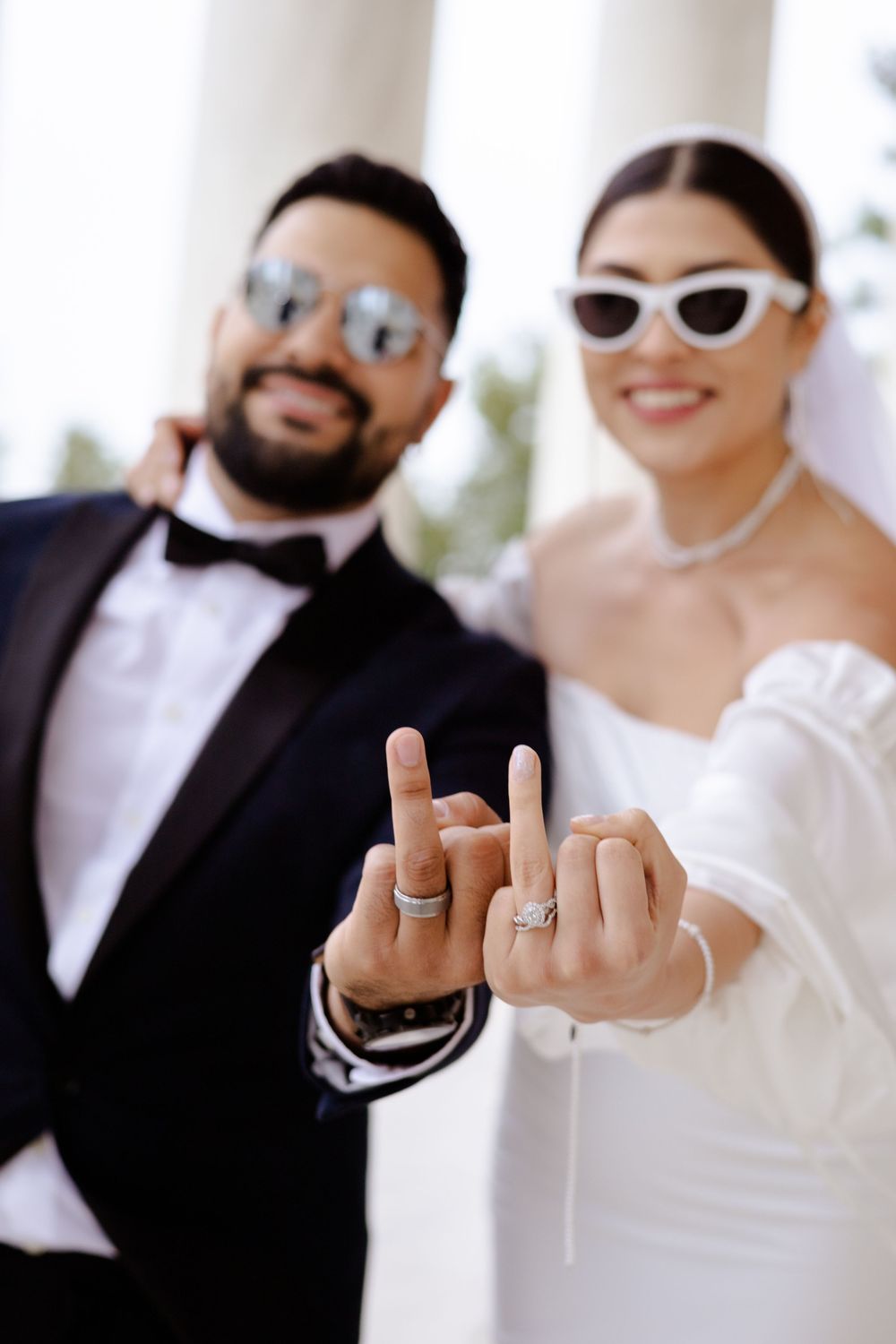 Playful wedding photo series showing couple in formal attire making silly hand gestures with white sunglasses.