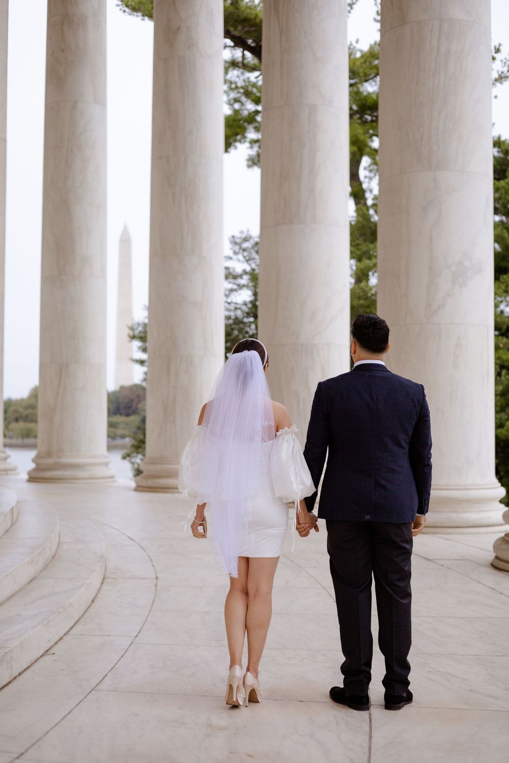 A bride and groom walk through a colonnade of white pillars in a series of four progressive shots.