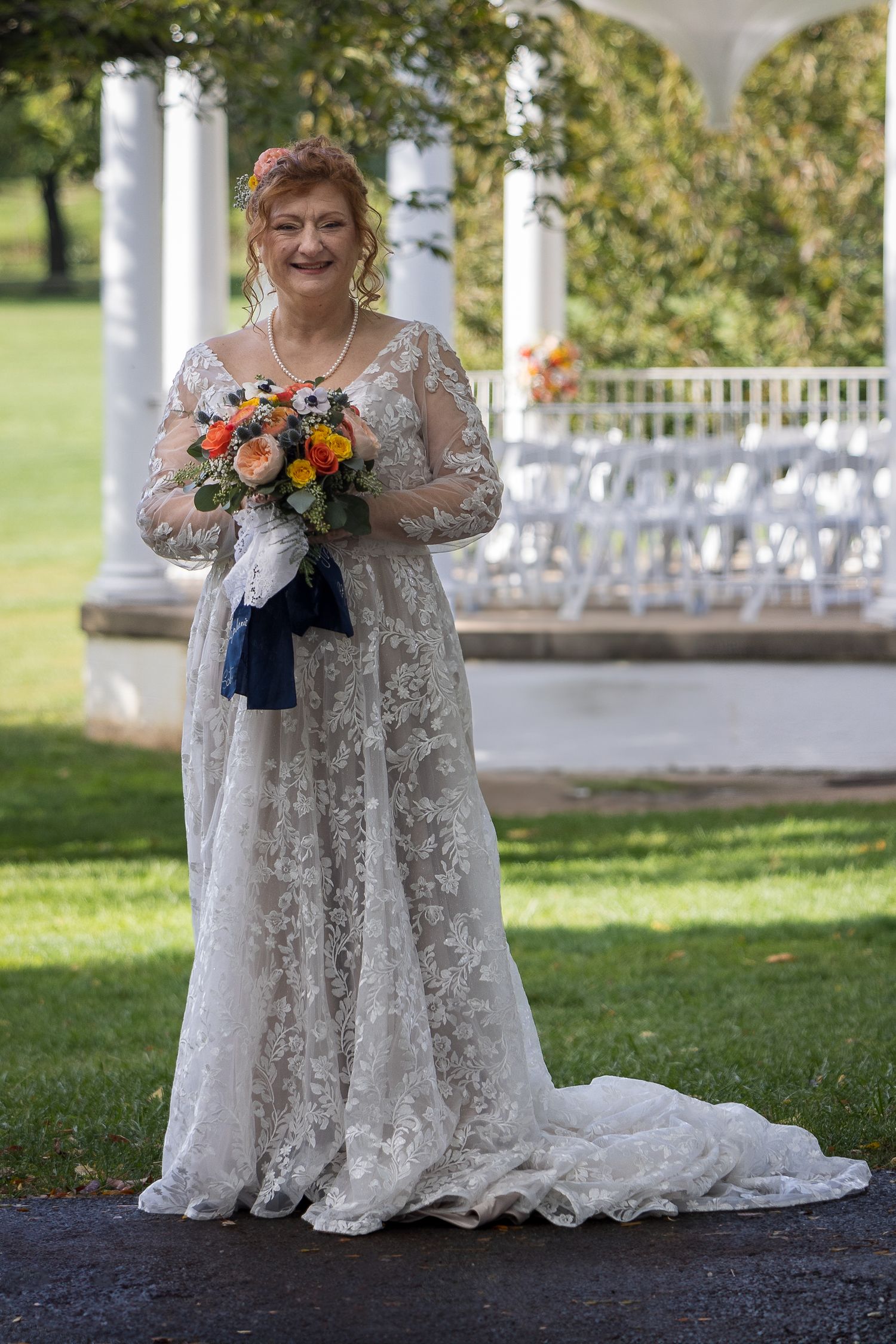 frederick maryland wedding photographer Bride in lace gown holds colorful bouquet in front of white columned pavilion with chairs.