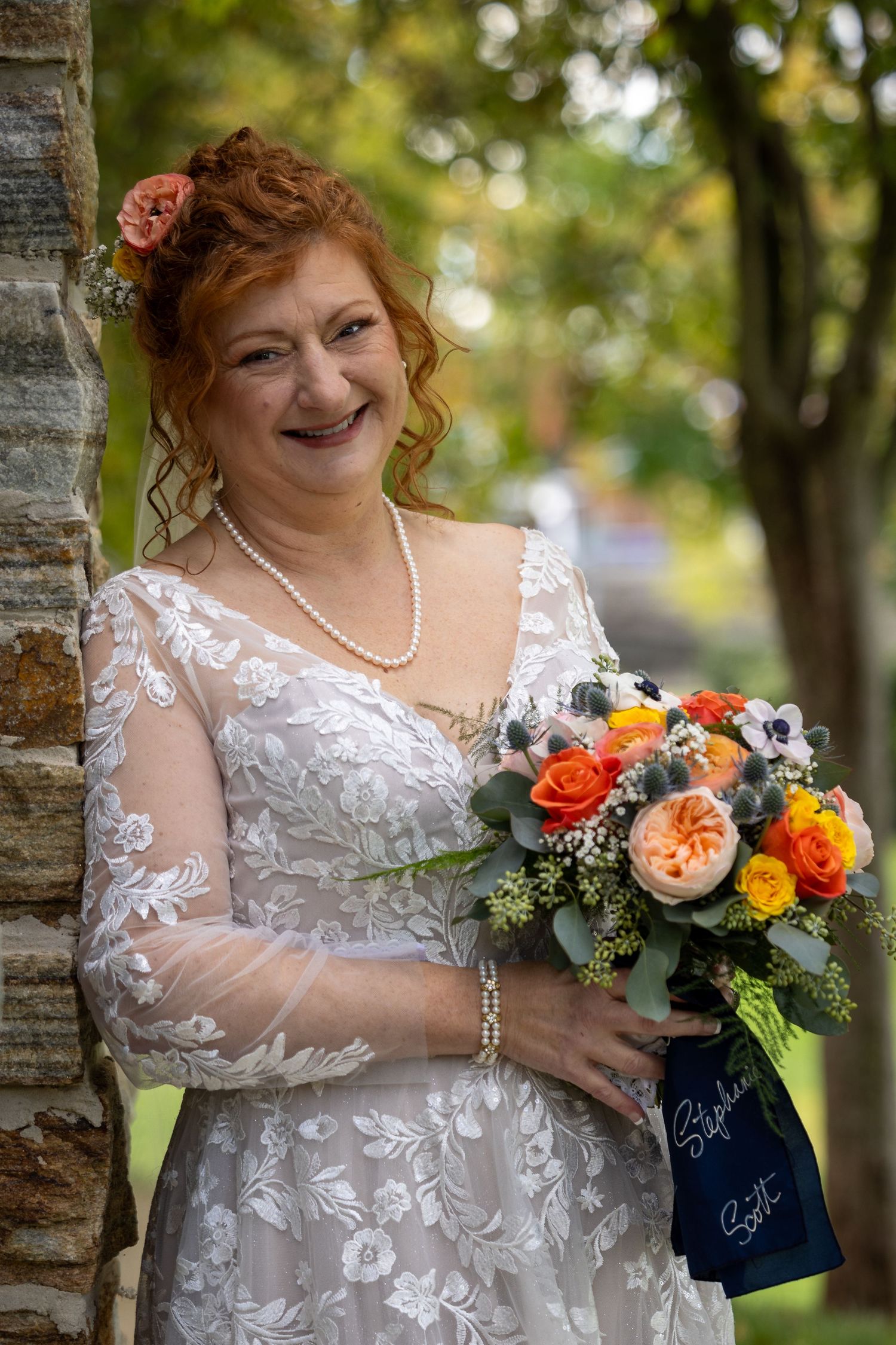 frederick maryland wedding photographer Bride with floral bouquet poses against tree in lace wedding gown and pearl necklace.