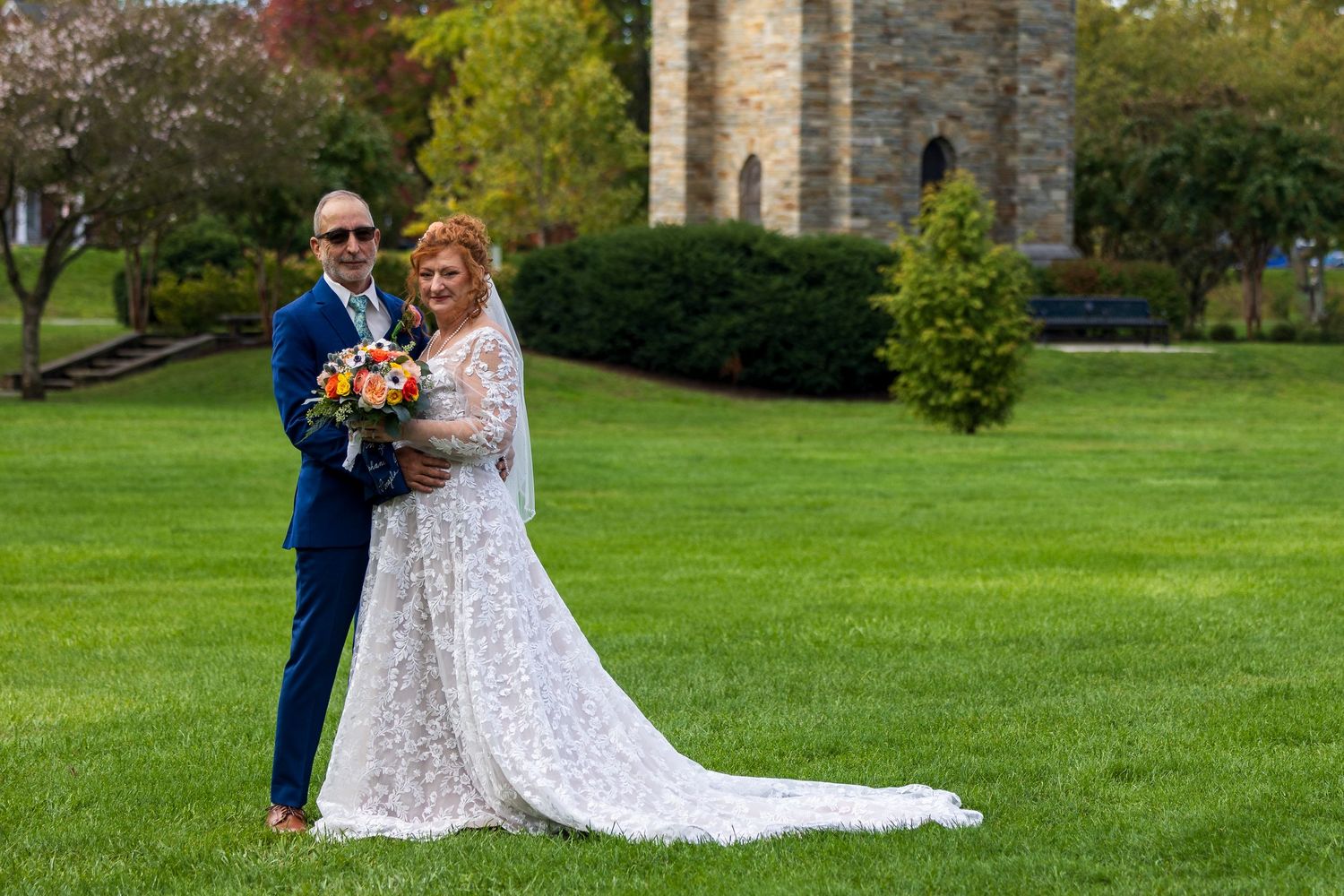 frederick maryland wedding photographer A wedding couple stands on a lush green lawn with a stone church tower in the background.