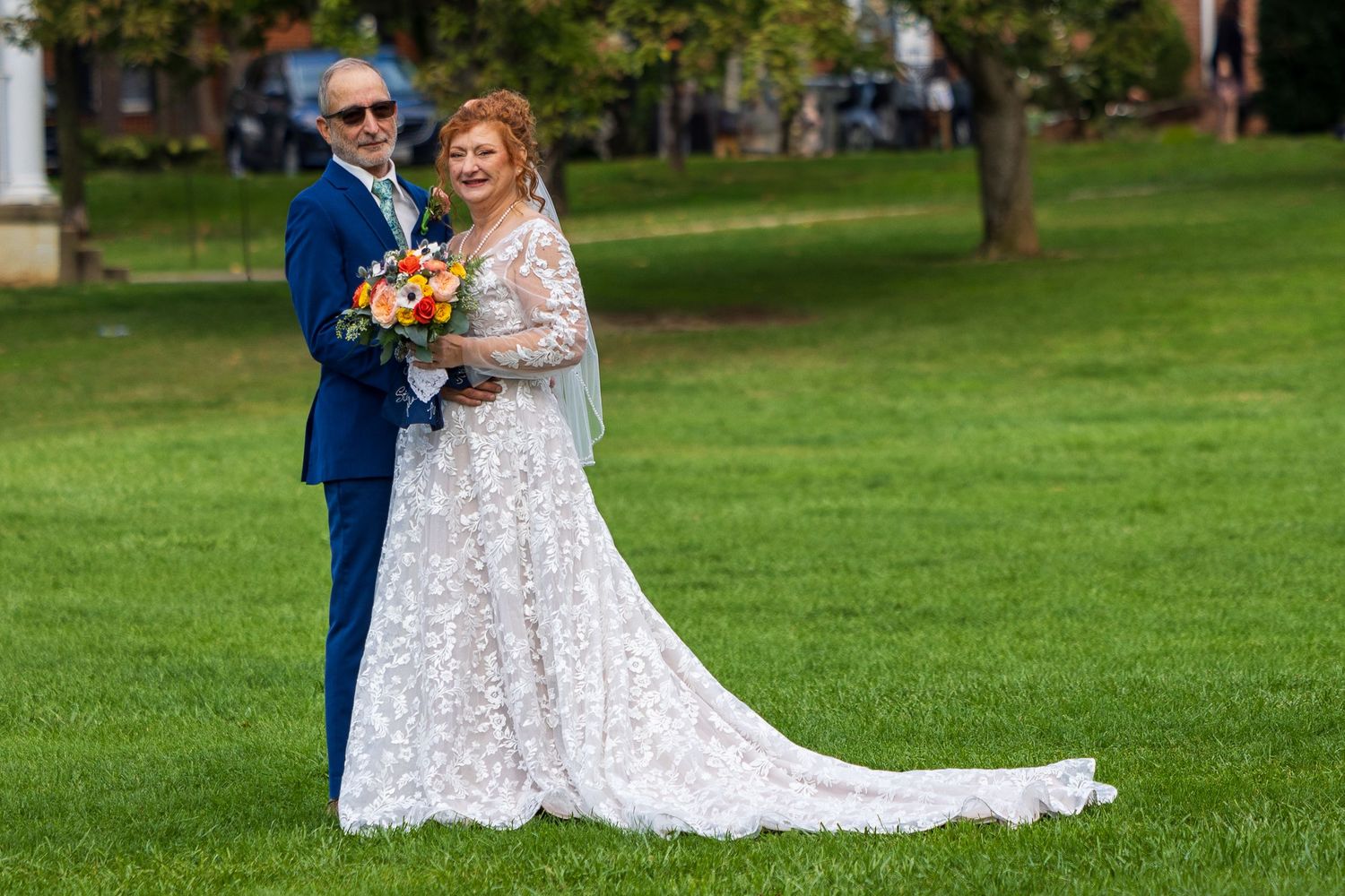 frederick maryland wedding photographer A wedding couple poses together on grass holding a vibrant orange and yellow bouquet.
