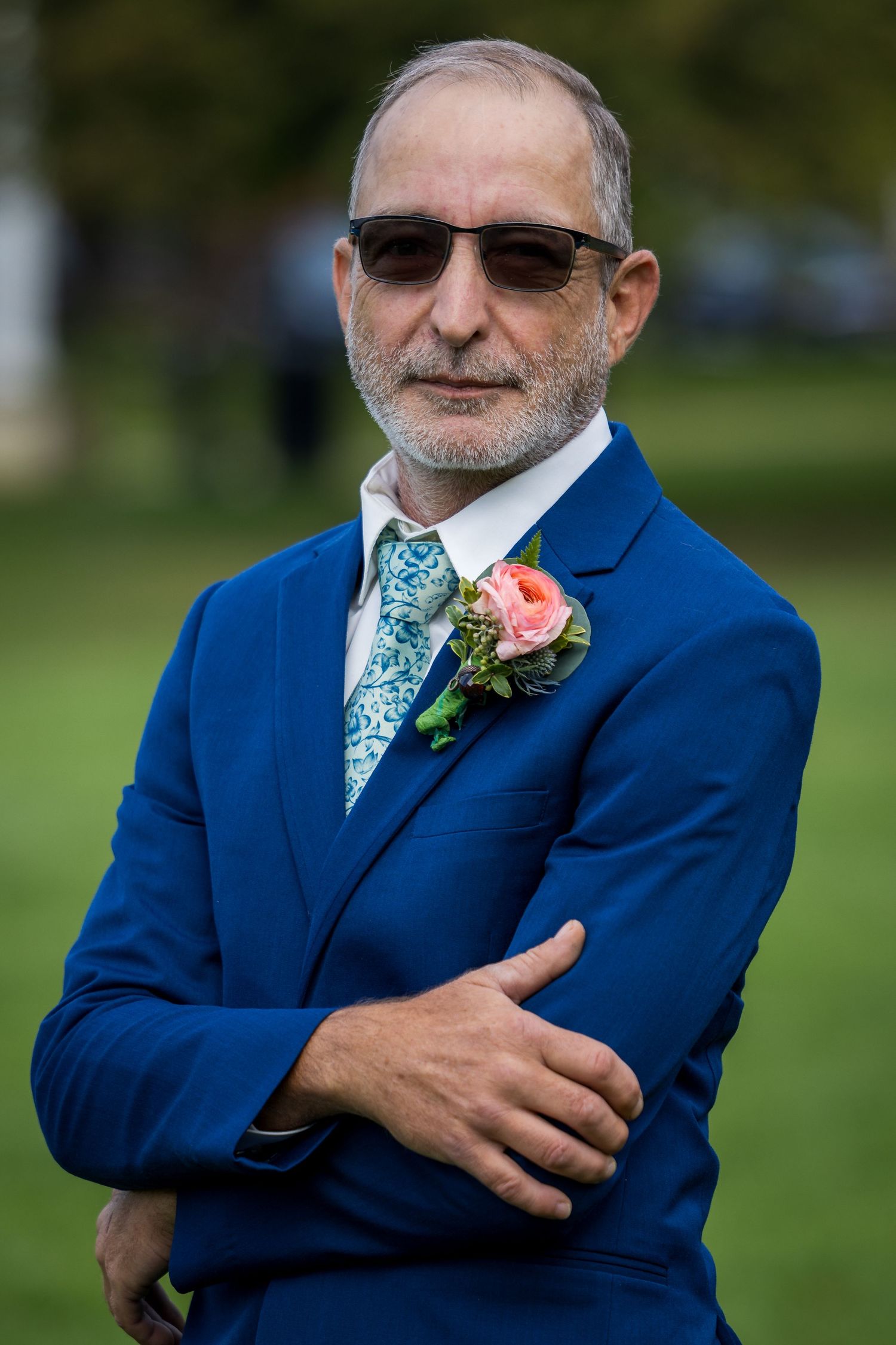 frederick maryland wedding photographerA groom in a navy suit with patterned tie and coral boutonniere poses outdoors.