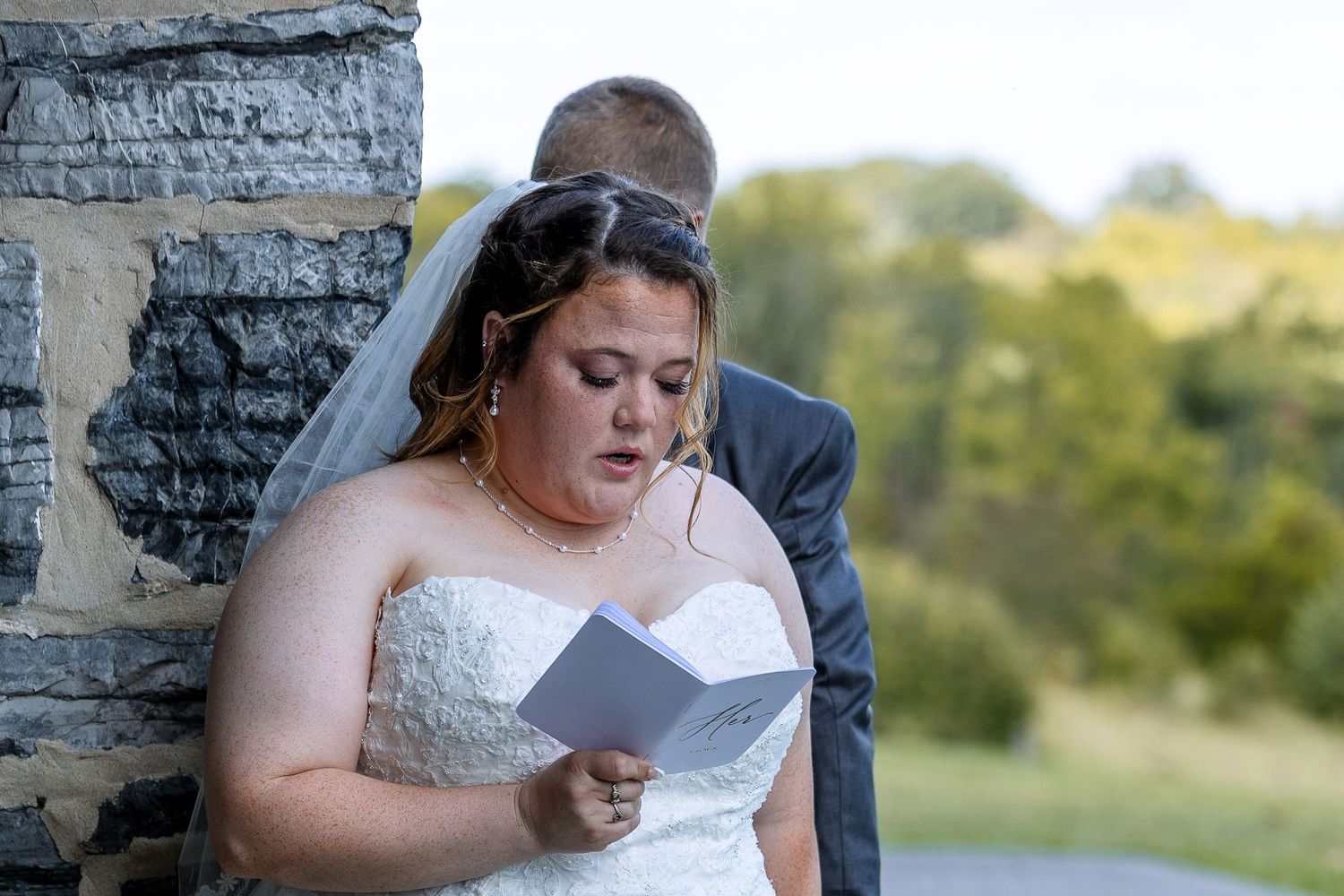 frederick maryland wedding photographer Person in wedding dress reading from paper against stone wall exterior.