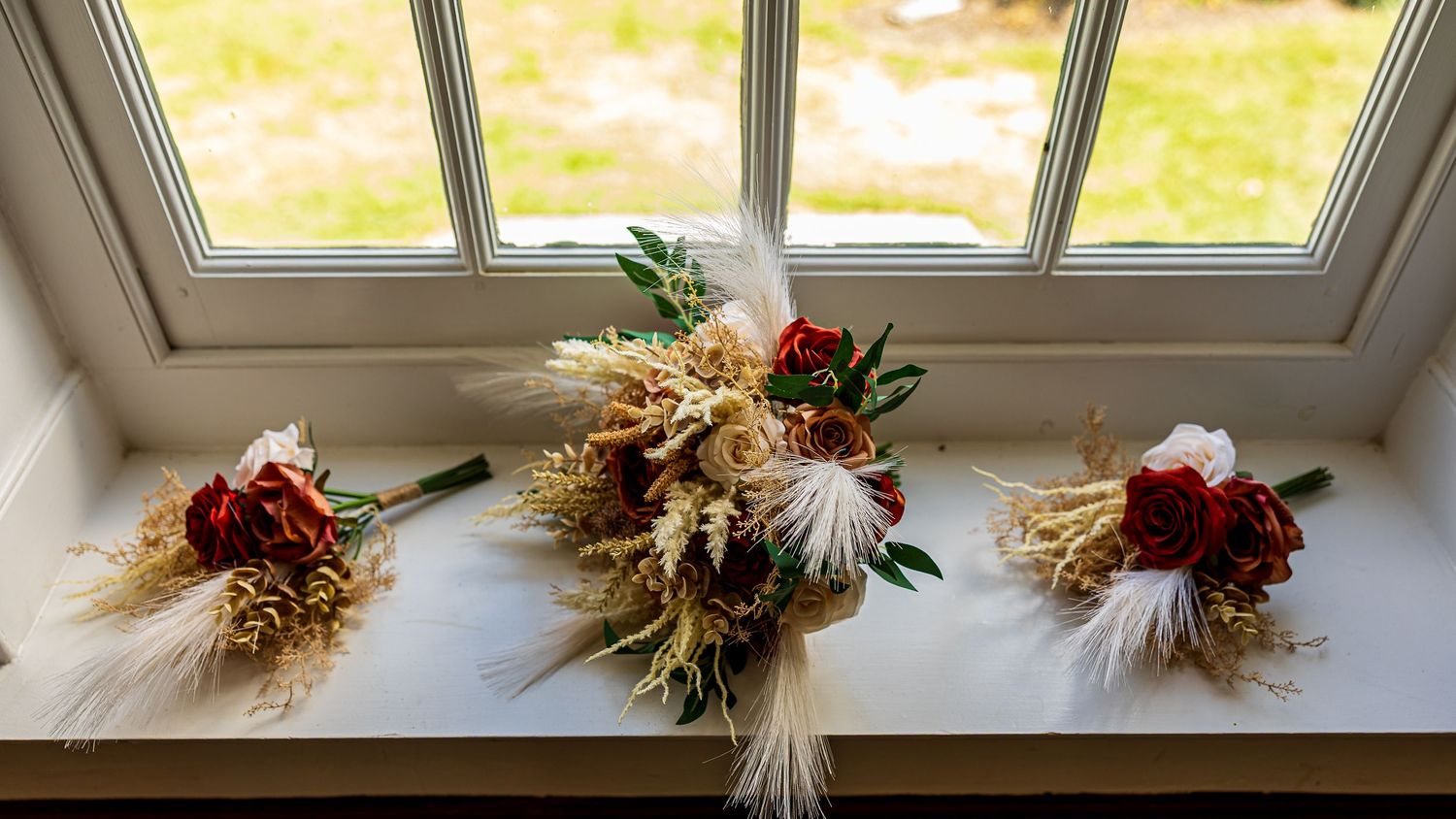 frederick maryland wedding photographer Three rustic wedding bouquets with dried flowers and wheat stalks displayed on a windowsill.
