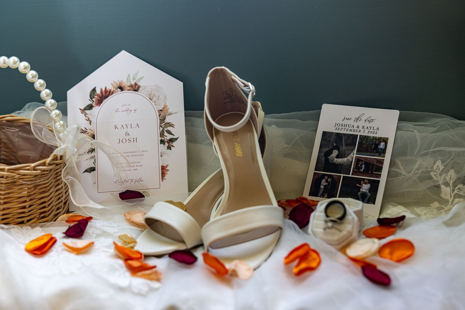 frederick maryland wedding photographer Wedding details including white heels, invitation, and scattered orange rose petals on white fabric.