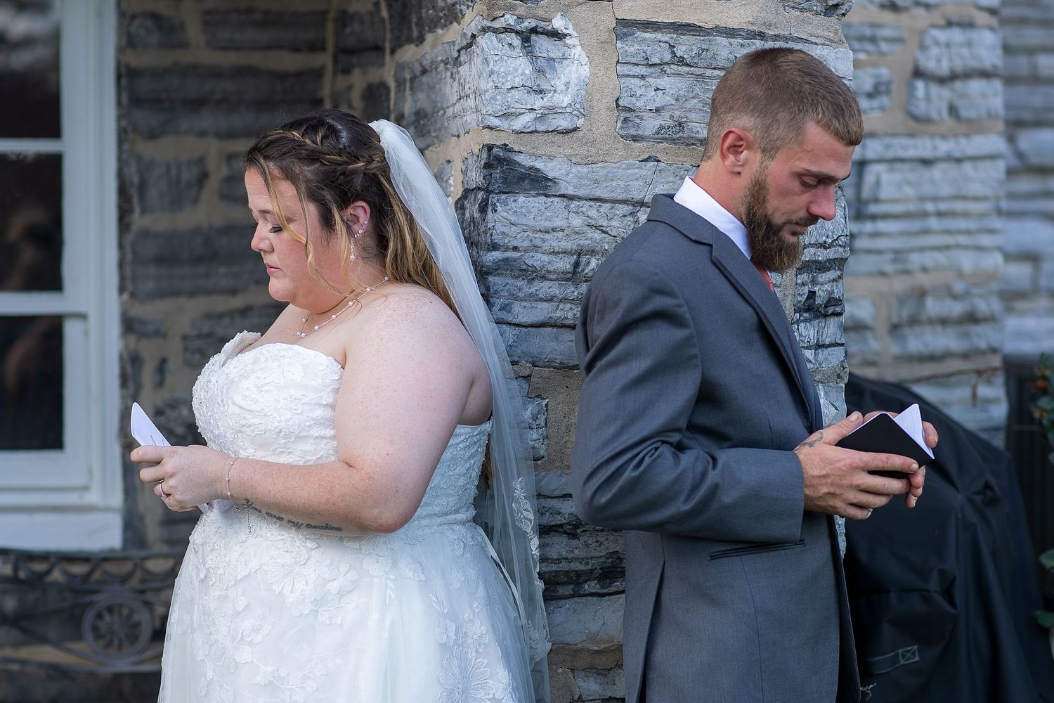 frederick maryland wedding photographer Couple in wedding attire checking their phones while standing against stone wall.