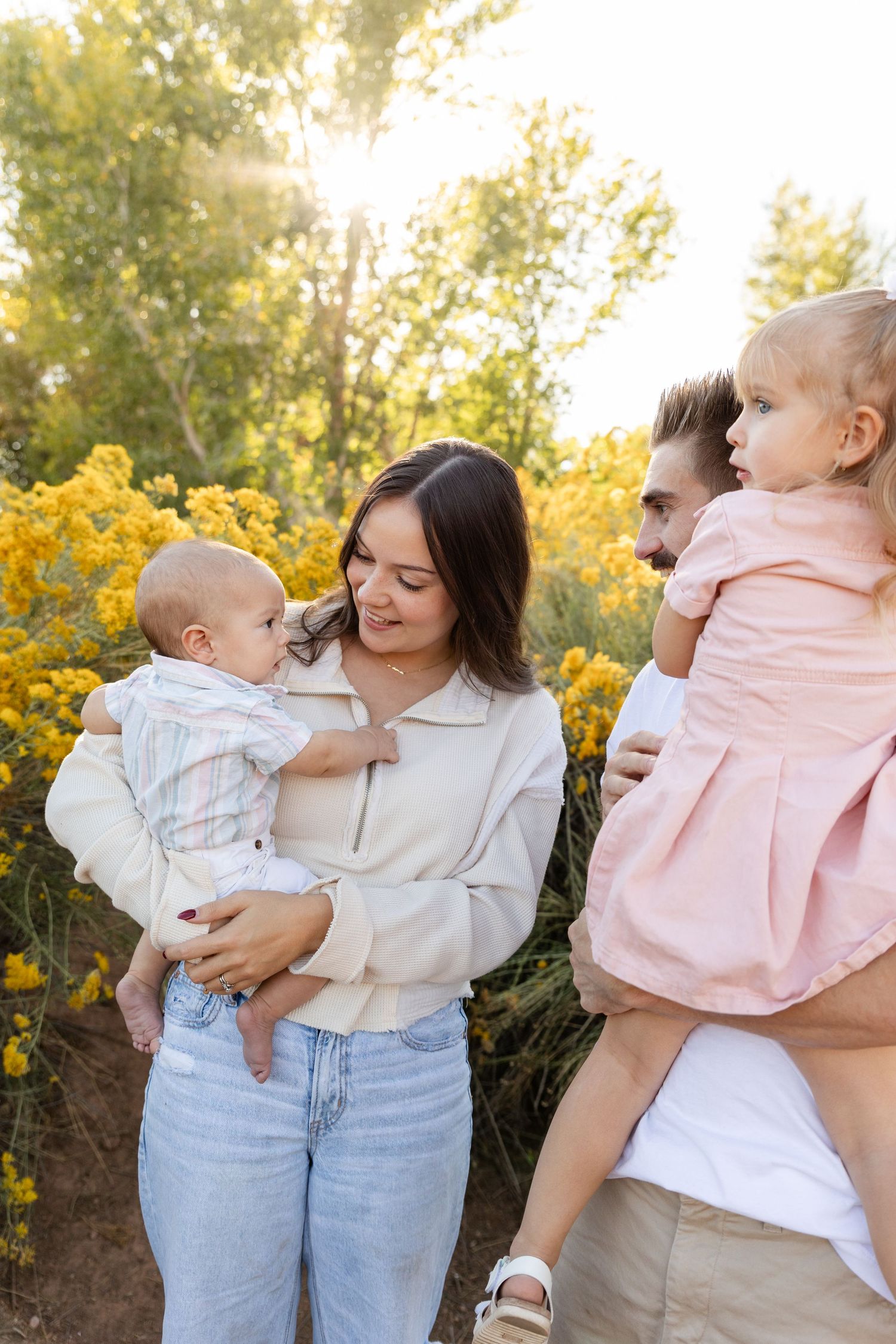 Happy young family with two small children enjoying a sunny day outdoors among yellow wildflowers.
