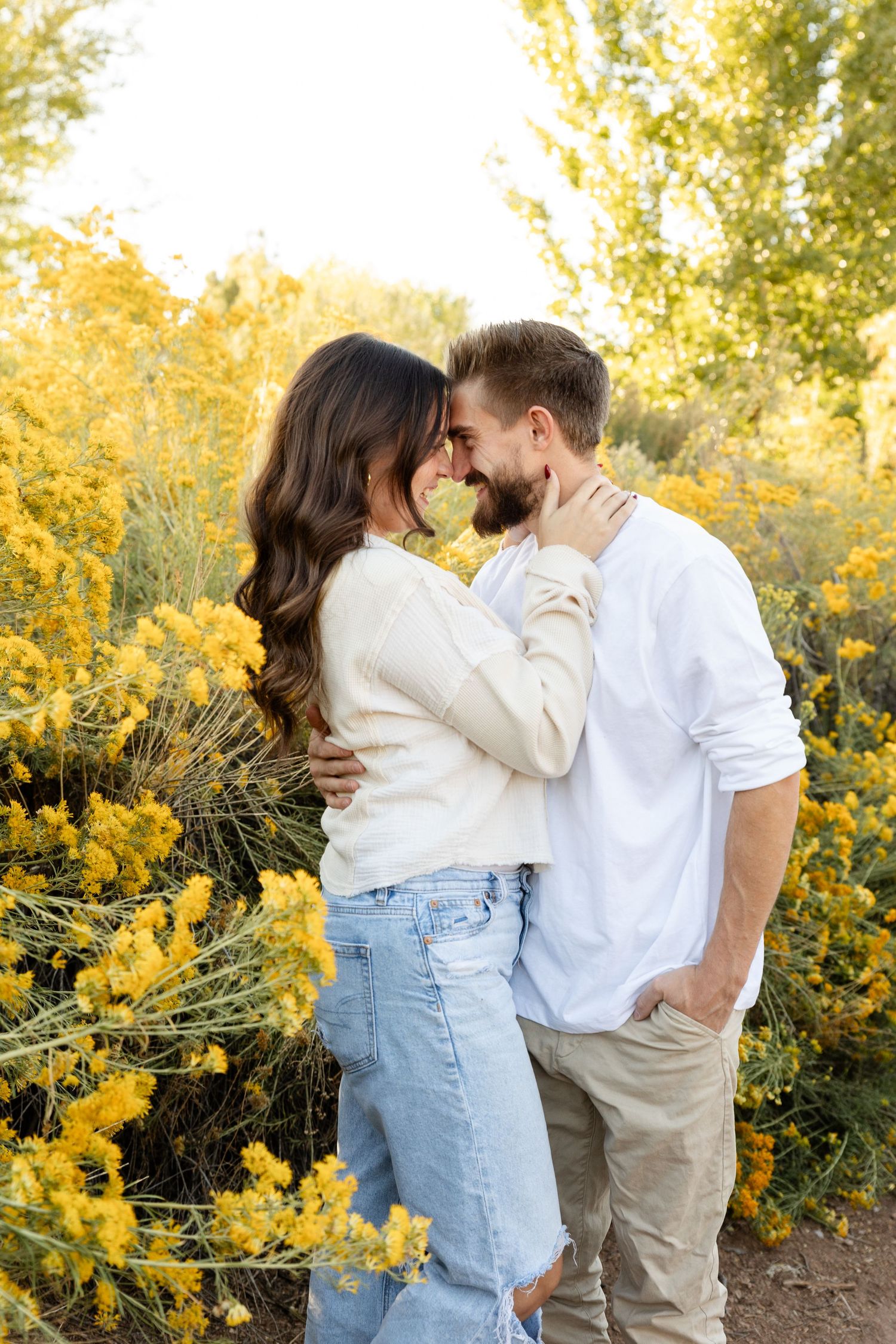 Romantic couple embracing and touching foreheads among vivid yellow wildflowers in warm sunset light.