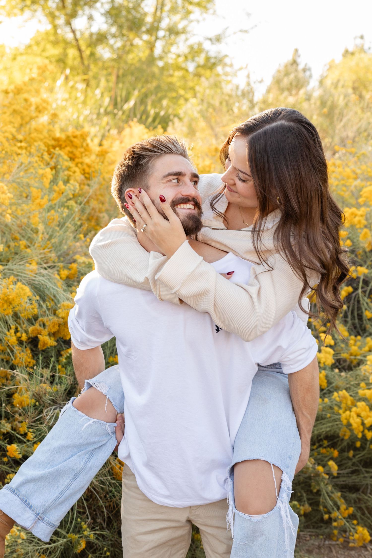 A couple shares a romantic piggyback ride among yellow wildflowers, smiling at each other in warm golden light. at tonaquint park st. George