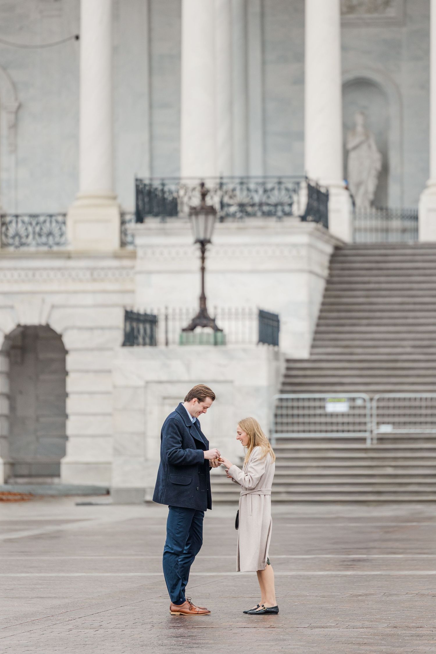 Two people share a romantic moment on the steps of a grand white marble building with classical architecture.