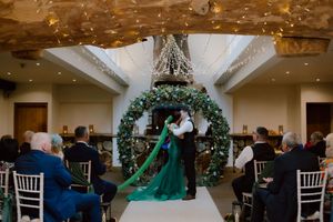 Wedding guests dance and celebrate on a dimly lit dance floor beneath elegant chandeliers at an indoor reception venue.