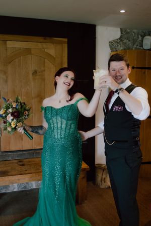 A couple dances together at a wedding reception, with the person in a sparkly emerald green dress and black formal attire.