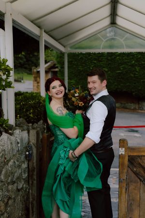 A couple in formal attire dances together under a white canopy, with the woman wearing a vibrant emerald green dress.